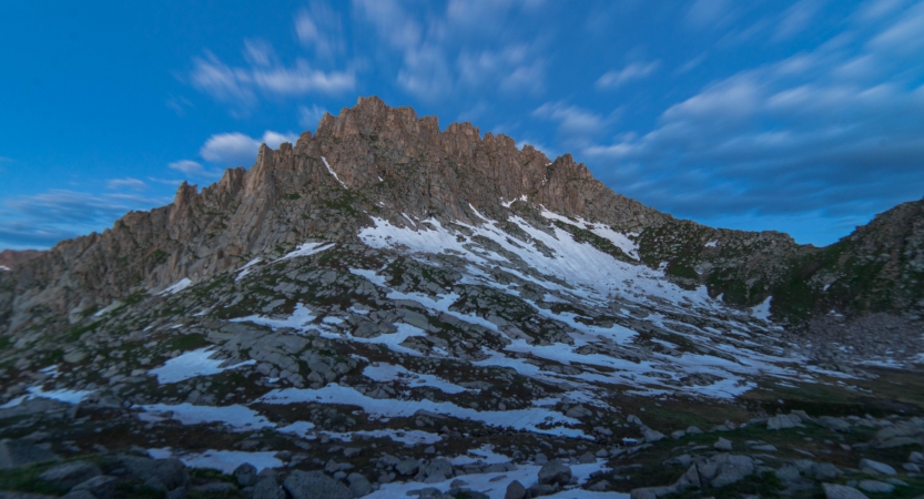 Snow dots a rocky mountain under a blue sky.